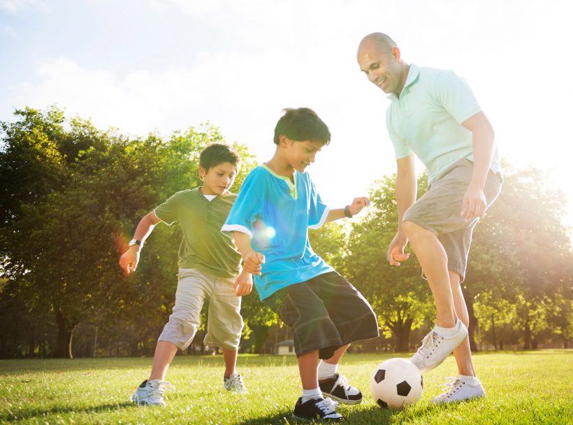man and two boys playing soccer in the park
