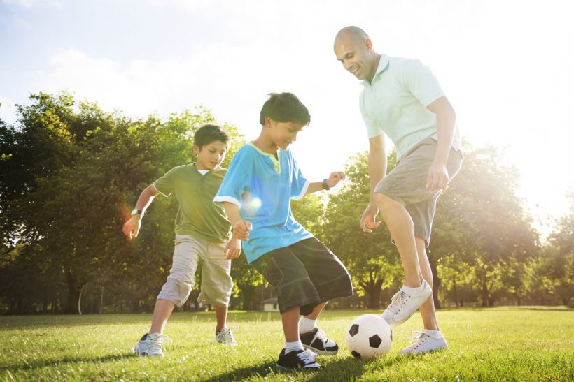 Man with 2 boys playing soccer in park